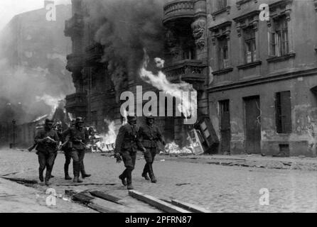 Im Januar 1943 kamen die nazis an, um die Juden des Warschauer Ghettos zu verhaften. Die Juden, die entschlossen waren, es zu bekämpfen, nahmen es mit selbstgemachten und primitiven Waffen auf die SS abgesehen. Die Verteidiger wurden hingerichtet oder deportiert, und das Ghetto-Gebiet wurde systematisch abgerissen. Dieses Ereignis ist bekannt als Ghetto-Aufstand. Dieses Bild zeigt eine Gruppe deutscher Soldaten, die die brennende Nowolpie Street entlanglaufen. Dieses Bild stammt aus der deutschen Fotoaufzeichnung des Ereignisses, bekannt als Stroop-Bericht. Stockfoto