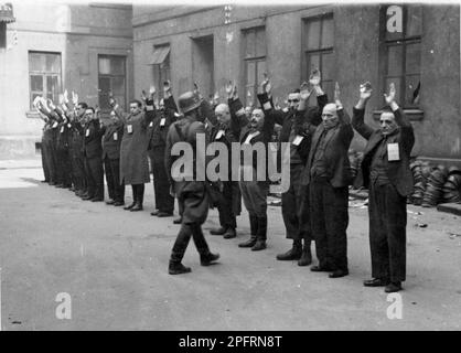 Im Januar 1943 kamen die nazis an, um die Juden des Warschauer Ghettos zu verhaften. Die Juden, die entschlossen waren, es zu bekämpfen, nahmen es mit selbstgemachten und primitiven Waffen auf die SS abgesehen. Die Verteidiger wurden hingerichtet oder deportiert, und das Ghetto-Gebiet wurde systematisch abgerissen. Dieses Ereignis ist bekannt als Ghetto-Aufstand. Dieses Bild zeigt eine SS-Truppe, die die Leiter der jüdischen Abteilung der Brauer-Helmfabrik festnimmt. Der Brauer „Hop“ von Herman Brouer stellte Helme für die deutsche Armee her und beschäftigte 2 Menschen. Ihre Arbeiter waren wahrscheinlich die letzten Juden, die aus dem Ghetto deportiert wurden. Dieses Bild ist vom G Stockfoto