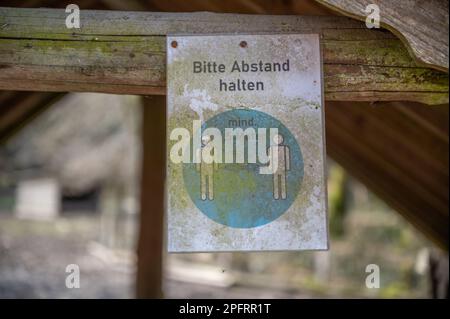 Halten Sie die Entfernung von 1,5 Metern ein deutsches Corona Covid-19-Regelschild mit Schmutz und Staub, das auf einem Holzgebäude in einem Vergnügungs-Safaripark hängt Stockfoto