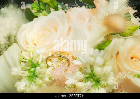 Goldene Eheringe liegen in grünem, weißem Hochzeitsstrauß mit frischen Blumen Stockfoto