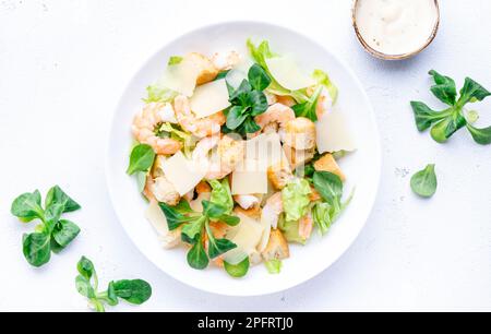 Caesar Salat mit Garnelen, Eisberg und Lammsalat, Croutons, Parmesan mit caesar Dressing. Weißer Tischhintergrund, Draufsicht Stockfoto
