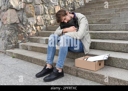 Ein junger Geschäftsmann wurde gefeuert. Er saß auf der Treppe und litt an schweren Depressionen. Arbeitslosenkonzept Stockfoto