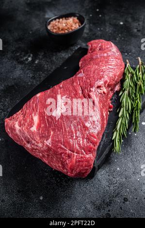 Rohes amerikanisches Tri-Tip-Rindfleisch auf Marmorbrett. Schwarzer Hintergrund. Draufsicht. Stockfoto