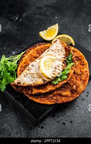 Traditionelle türkische Pizza mit Lahmacun und Salat auf Marmorbrett mit Gewürzen. Schwarzer Hintergrund. Draufsicht. Stockfoto