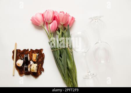 Sushi und Weingläser und rosa Tulpen auf weißem Hintergrund, Weihnachtsessen Stockfoto