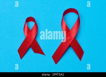 Ein seidenrotes Band in Form einer Schleife auf blauem Hintergrund, ein Symbol für den Kampf gegen AIDS und ein Zeichen der Solidarität und Unterstützung Stockfoto