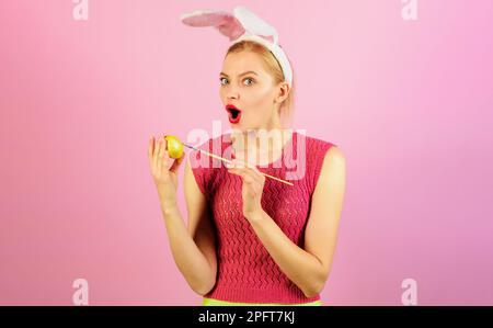 Frohen Ostertag. Überraschte Frau mit Häschenohren, die Ostern Ei malt. Hasenmädchen mit gelbem Ei. Rabatt. Ostereier-Dekorationsideen Stockfoto