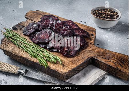 Geschnittene, pferdgetrocknete Wurst auf Wooodenbrett mit Kräutern. Grauer Hintergrund. Draufsicht. Stockfoto