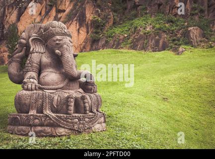 Ganesha Statue aus Stein, mit einem wunderschönen Garten im Hintergrund Stockfoto