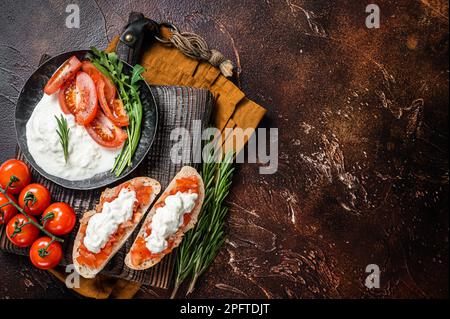 Bruschettas mit Stracciatella-Käse, gehackten Kirschtomaten und Rosmarin. Dunkler Hintergrund. Draufsicht. Speicherplatz kopieren. Stockfoto