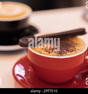 Schokoladen-Cappuccino in einem roten Becher mit einem Schokoladenlöffel. Ein schwarzes Weiß in der Szene. Stockfoto