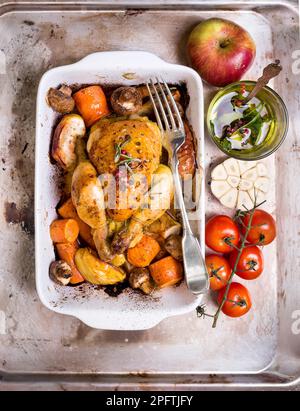 Köstliches gebackenes saftiges Hähnchen mit goldknuspriger Haut. Gebratenes Hähnchen in Backform mit Äpfeln, Karotten, Pilzen, Rosmarin, Knoblauch, Pfeffer auf Stockfoto