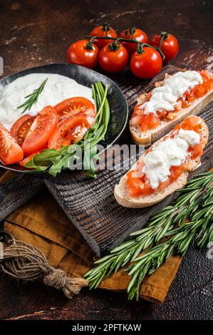 Bruschettas mit Stracciatella-Käse, gehackten Kirschtomaten und Rosmarin. Dunkler Hintergrund. Draufsicht. Stockfoto