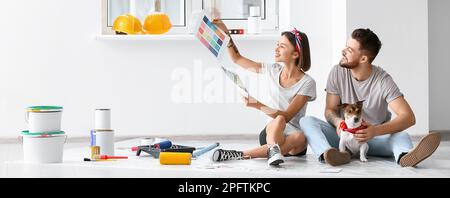 Glückliches junges Paar mit niedlichem Hund, das Farbe für die Reparatur in seinem neuen Haus aussucht Stockfoto