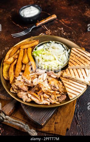 Türkischer Döner Kebab oder Gyros auf einem Teller mit pommes Frites, Gemüse und Salat. Dunkler Hintergrund. Draufsicht. Stockfoto