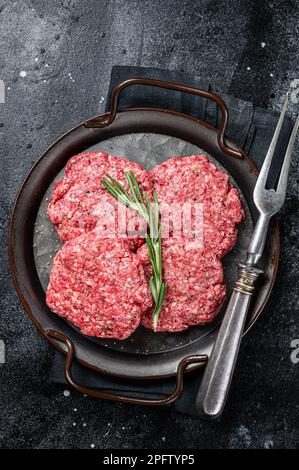 Ungekochte Frikadellen aus Hackfleisch, rohe Fleischschnitzel. Schwarzer Hintergrund. Draufsicht. Stockfoto