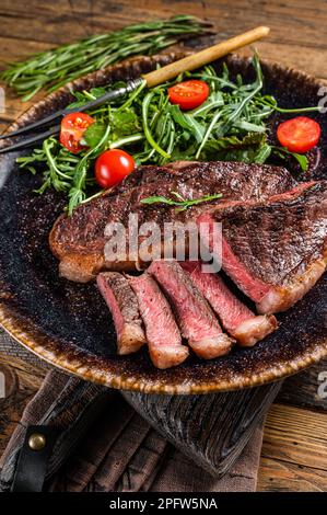 BBQ gegrilltes Rumpsteak in Teller mit Gemüsesalat. Holzhintergrund. Draufsicht. Stockfoto