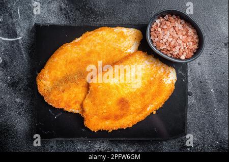 Gebratene panierte Tilapia-Filets auf einem Marmorbrett. Schwarzer Hintergrund. Draufsicht. Stockfoto