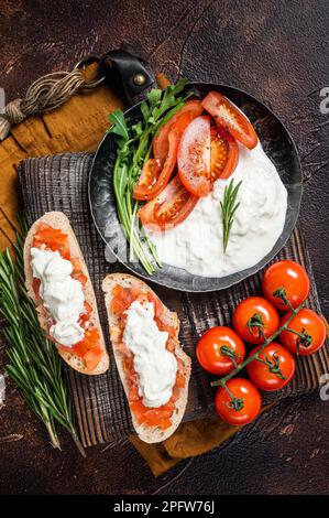 Bruschettas mit Stracciatella-Käse, gehackten Kirschtomaten und Rosmarin. Dunkler Hintergrund. Draufsicht. Stockfoto