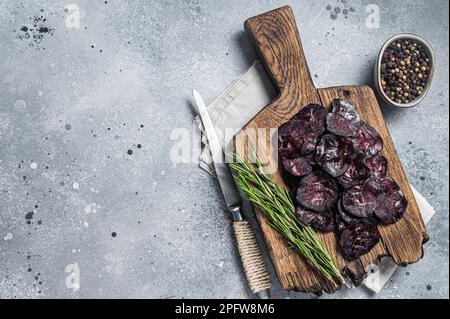 Geschnittene, pferdgetrocknete Wurst auf Wooodenbrett mit Kräutern. Grauer Hintergrund. Draufsicht. Speicherplatz kopieren. Stockfoto