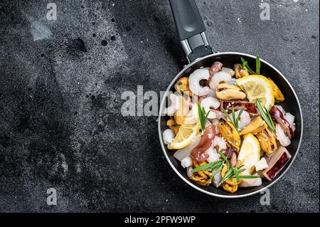 Roher Mix aus Meeresfrüchten mit Garnelen, Garnelen, Muscheln, Tintenfisch und Tintenfisch in einer Pfanne, die zum Kochen bereit ist. Schwarzer Hintergrund. Draufsicht. Speicherplatz kopieren. Stockfoto