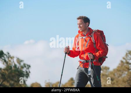 Männliche Wanderer wandern auf dem Bergpfad am Sommertag im Freien und tragen Oberbekleidung Jacke und Rucksack zum Campen. Ein Typ porträtiert den Lebensstil, mit dem er spazieren geht Stockfoto