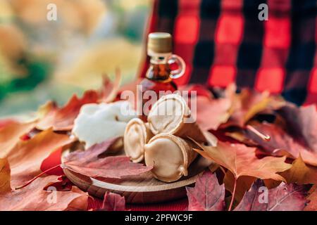 Ahornsirup Taffy Cones Dessert mit traditioneller Flasche und kariertem Stofftisch - rote Blätter auf dem Tisch. Einheimisches Essen aus Quebec. Stockfoto