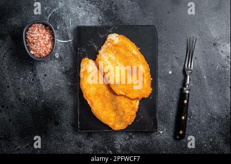 Gebratene panierte Tilapia-Filets auf einem Marmorbrett. Schwarzer Hintergrund. Draufsicht. Stockfoto