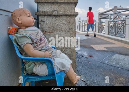 Am Phra Arthit Pier am Chao Phraya River, Bangkok, Thailand, hat jemand die Puppe eines Jungen auf einen Stuhl gelegt und ihm eine Zigarette in den Mund gesteckt Stockfoto