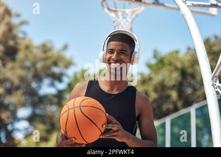 Basketball ist eine hervorragende Möglichkeit, um in Form zu kommen und aktiv zu bleiben. Ein sportlicher junger Mann, der Musik hört, während er Basketball auf einem Sportplatz spielt. Stockfoto