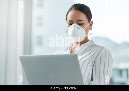 Wir sehen uns wieder, online. Eine maskierte junge Geschäftsfrau, die ein Notebook in einem modernen Büro benutzt. Stockfoto