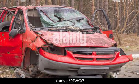 Rostiges und kaputtes rotes verlassenes Auto auf der Straße der Stadt. Ein verlassener Autounfall draußen. Altes, verlassenes rostiges Auto ohne Räder an der Seite des Stockfoto