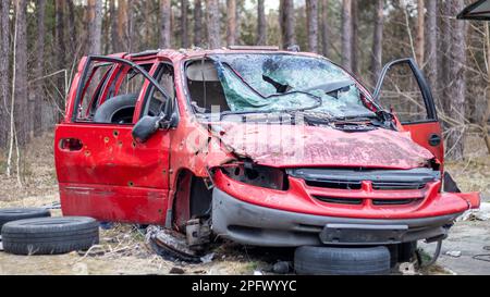 Rostiges und kaputtes rotes verlassenes Auto auf der Straße der Stadt. Ein verlassener Autounfall draußen. Altes, verlassenes rostiges Auto ohne Räder an der Seite des Stockfoto