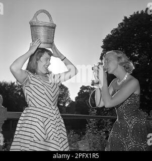 Fotograf in den 1950er. Eine junge Frau fotografiert an einem Sommertag. Eine Freundin von ihr posiert für sie und hält einen Korb über ihrem Kopf. Schweden 1951. Conard Ref. 1752 Stockfoto