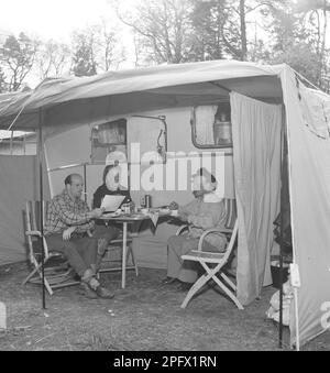 1950er Uhr Camping. Drei Personen sitzen neben ihrem Wohnwagen und genießen eine Tasse Kaffee. Die Nutzung von Wohnwagen für den Sommerurlaub war zu dieser Zeit recht neu. Schweden Juli 1953. Kristoffersson Ref. BP30-9 Stockfoto