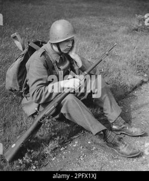 Soldat in den 1940er. Ein Mann in Uniform, Gewehr und Paket sieht müde aus, wenn er auf dem Boden sitzt und seinen Kopf auf seinem Arm ruht. Schweden 1942 Stockfoto