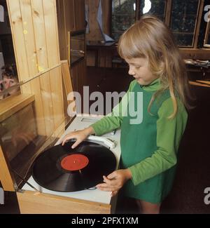 Ein Mädchen steht vor einem Grammophon, das mit Klas Klättermus eine LP spielen wird. Die Schallplatte des Vinyl-Grammophons war besser als die ältere, so genannte 78-U/min-Schallplatte. Sie wurde auch mit einer niedrigeren Geschwindigkeit und mit dichteren Titeln wiedergegeben, was bedeutete, dass die Wiedergabezeit der Discs deutlich länger war als zuvor. Die Grammophon-Schallplatte war das Medium, das die Veröffentlichung der Musik während des fast gesamten 20. Jahrhunderts dominierte. In den 1990er Jahren wurde die CD dominierend, wobei eine hundert Jahre alte Technologie der mechanischen Tonspeicherung fast vollständig durch digitale Speicherung ersetzt wurde. Die heutigen Musikliebhaber verwenden str Stockfoto