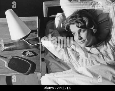 Schlafen Sie im 1960er. Eine junge Frau liegt bequem in einem Bett. Auf dem Nachttisch befindet sich eine kleine Leselampe und ein Glas Wasser. Schweden 1960 Stockfoto