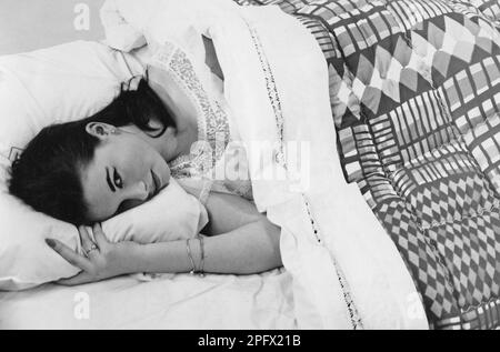 Frau im Bett. Eine Frau liegt in einem Bett, in Bettwäsche und Decke, entworfen von Irene Flycht, einem preisgekrönten Design 1956. Stockfoto