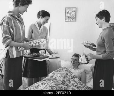 Geburtstag in den 1960er. Eine junge Frau liegt im Bett und ist überrascht, dass ihre Freundinnen dir alles gute zum Geburtstag singen. Sie haben alle drei Geschenkpapiere fertig. Ein Kaffeetablett und Kaffee aus einer silbernen Kanne und Kuchen sind ebenfalls im Preis enthalten. Schweden 1961 Stockfoto