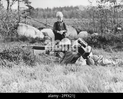 Der zweite Weltkrieg steht bevor. Schweden rüstet die Verteidigung aus und übt im Herbst 1938 in Småland. Ein Soldat liegt feldähnlich in der Natur von Småland und zielt mit seinem Gewehr. Ein kleiner Junge steht an der Seite und sieht wundervoll zu. 18. September 1938 Stockfoto