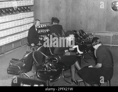 Einkaufen in der 1940er. Eine junge Frau in einem Damenschuhladen, wo sie Schuhe ausprobiert. Die freundliche und geduldige Verkäuferin hilft ihr und scheint es nicht zu stören, dass sie so viele verschiedene Paar Schuhe ausprobiert. Schweden 1942 Stockfoto