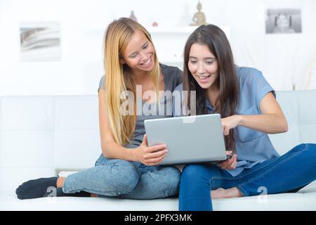 Zwei lächelnde Freundinnen, die auf dem Sofa sitzen und Hausaufgaben machen Stockfoto