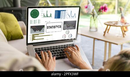 Die Analystin an ihrem Schreibtisch arbeitet an einem Laptop, der Statistiken, Diagramme und Diagramme zeigt. Sie arbeitet am Holztisch im Kreativbüro. Über die Stockfoto