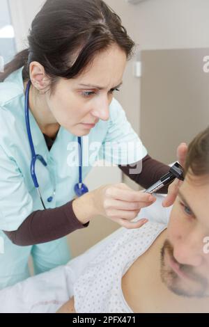 hno-Arzt schaut mit einem Instrument in das Ohr des Patienten Stockfoto