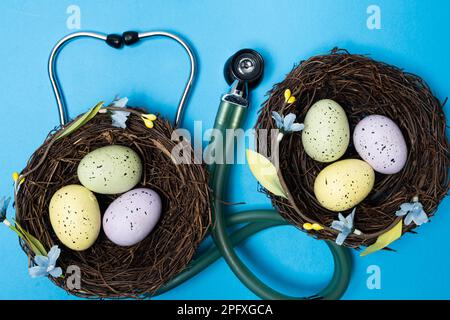 Ostermedizin. Zwei Nester mit bemalten Eiern und ein Stethoskop auf blauem Hintergrund Stockfoto