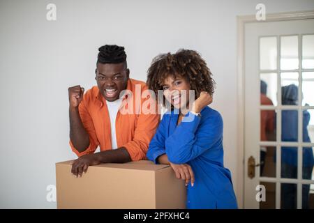 Aufgeregte Schwarze Ehepartner, Die An Der Pappschachtel Sitzen Und Ihren Erfolg Feiern Stockfoto