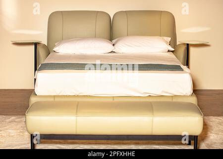 In warmen Pastelltönen gehaltene Innenausstattung mit Doppelbett und einem Kopfteil aus weichem Leder und Regalen an den Seiten. Stockfoto