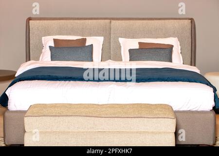 Doppelbett mit einem Kopfteil aus weichem Stoff in Beige und blauer Samtdecke. Stockfoto