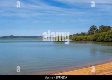 Blick vom Strand in Redland Bay über das wunderschöne, ruhige Wasser der Moreton Bay mit Autofähre in der Ferne und Inseln am Horizont Stockfoto